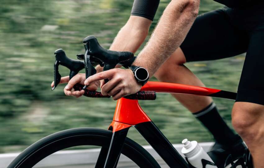 Person auf einem Fahrrad mit Fitness-Watch am Handgelenk, die aktuelle Sportstech Trends in vernetztem Training und Performance-Tracking zeigt.