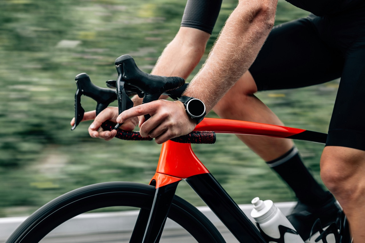 Person auf einem Fahrrad mit Fitness-Watch am Handgelenk, die aktuelle Sportstech Trends in vernetztem Training und Performance-Tracking zeigt.