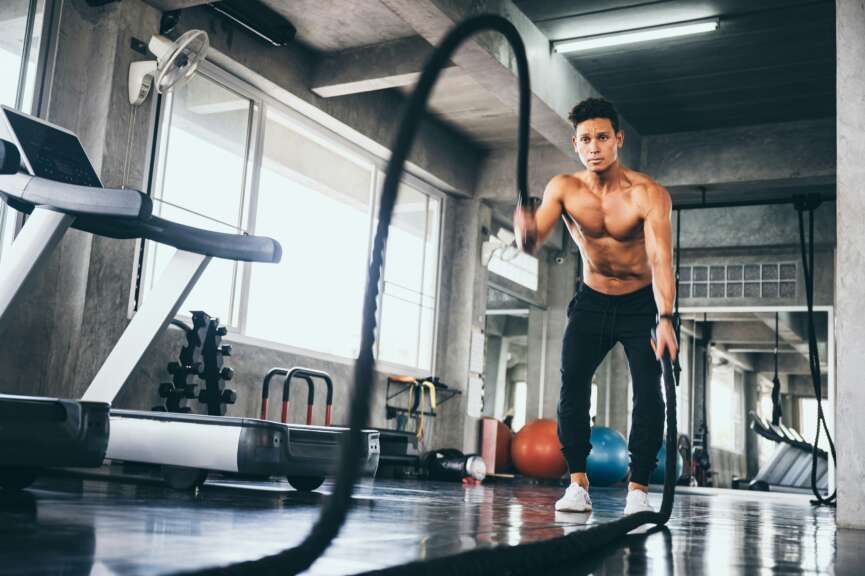 Ein Sportler testet seine Trainingsleistung in einem Fitnessstudio, w&auml;hrend er w&auml;hrend einer intensiven Trainingseinheit Battle Ropes verwendet.