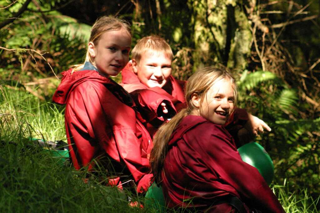 Three young people wearing waterproof jackets during an outdoor activity in a wooded area.