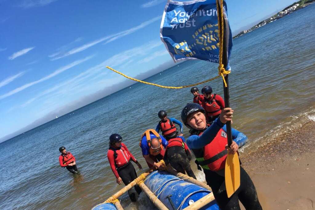 Young people and instructors building and launching a raft by the water during a Youth Adventure Trust activity.